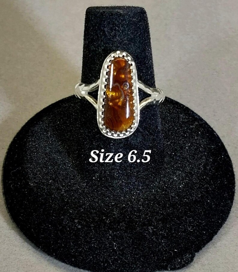 May include: A silver ring with a brown and gold oval gemstone set in a silver bezel. The ring is size 6.5.