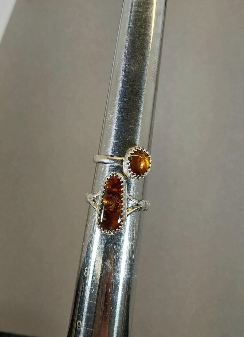 May include: Two silver rings with amber stones. The ring on the bottom has a rectangular stone, while the ring on top has a round stone.