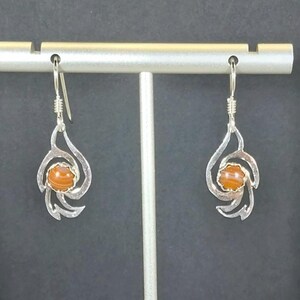 May include: A pair of silver dangle earrings with a swirl design and a brown agate stone in the center.