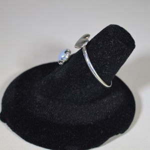May include: A silver ring with a heart-shaped design and a blue stone. The ring is displayed on a black velvet ring holder.