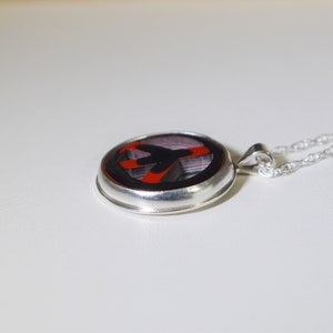 May include: A silver necklace with a round pendant featuring a black and red abstract design. The pendant is set in a silver bezel.