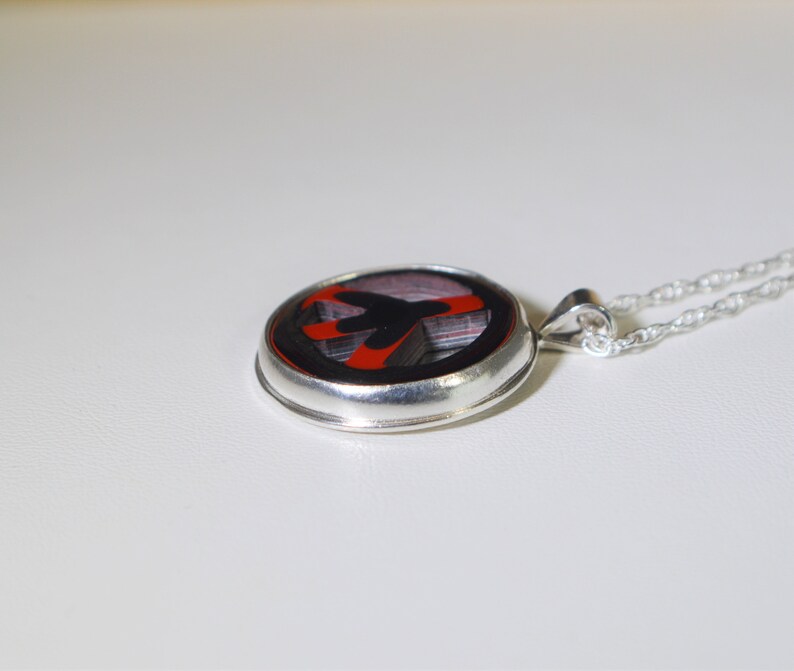 May include: A silver necklace with a round pendant featuring a black and red abstract design. The pendant is set in a silver bezel.