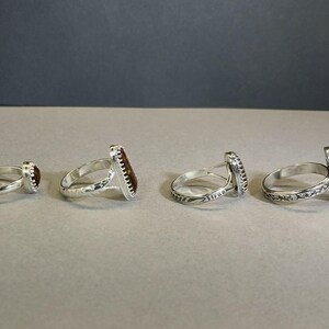 May include: Four silver rings with different colored stones. The rings are all set with a single stone, and the stones are all different shapes and sizes.