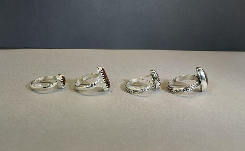 May include: Four silver rings with different colored stones. The rings are all set with a single stone, and the stones are all different shapes and sizes.