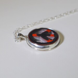 May include: A silver necklace with a round pendant featuring a red and black peace sign design.