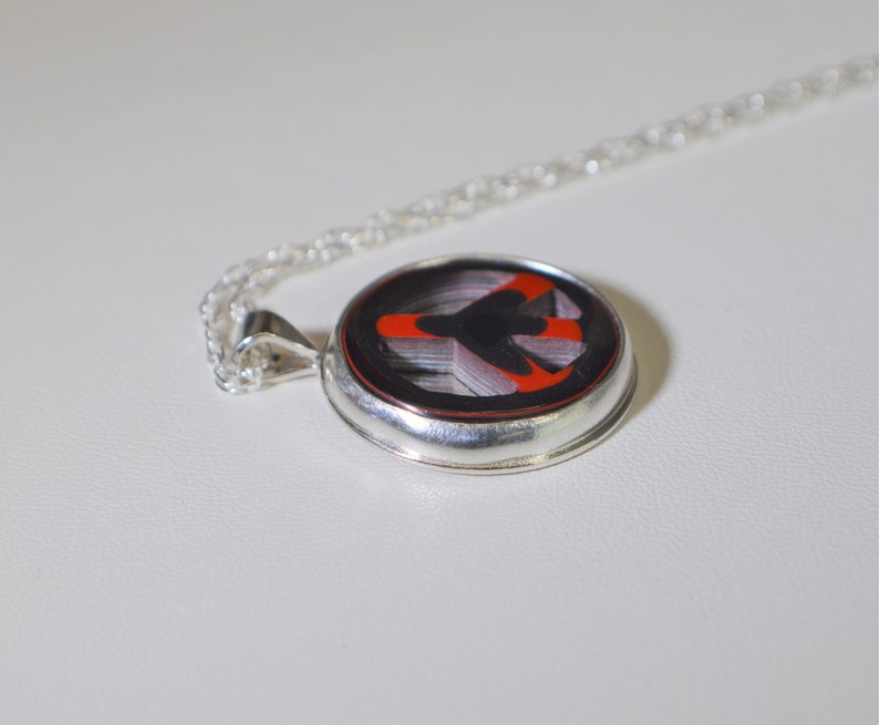 May include: A silver necklace with a round pendant featuring a red and black peace sign design.