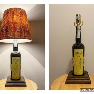 May include: A unique table lamp crafted from a Colonel E.H. Taylor whiskey bottle. The lamp features a dark brown lampshade with a textured pattern and a wooden base. The bottle has a yellow label with black text.