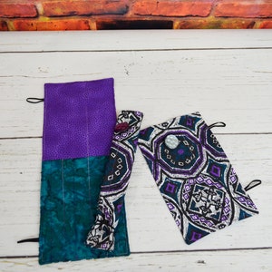 May include: Two fabric pencil cases with a purple and teal patterned design. One case is rolled up and the other is flat. Both cases have a button closure.