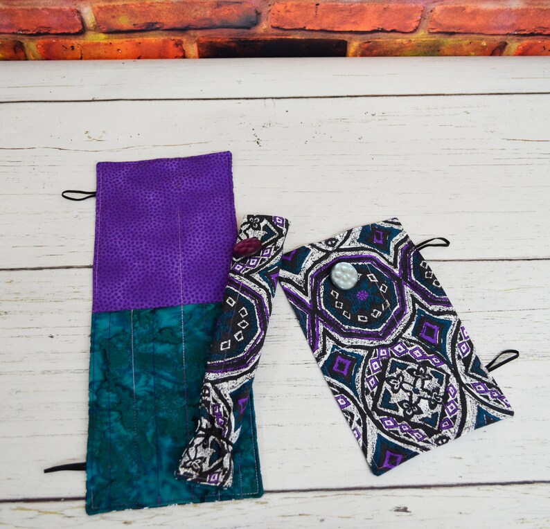 May include: Two fabric pencil cases with a purple and teal patterned design. One case is rolled up and the other is flat. Both cases have a button closure.