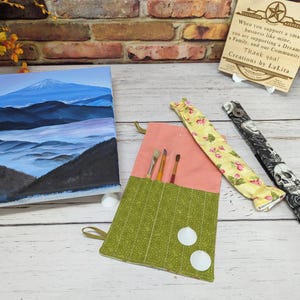 May include: A set of three handmade pencil cases. The first case is green with white polka dots and has two white buttons. The second case is pink with a floral pattern. The third case is black with a skull and rose pattern.