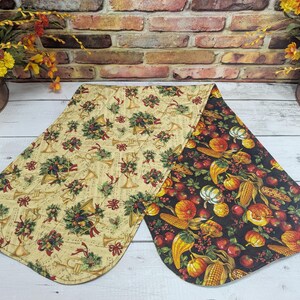 May include: A reversible table runner with a festive holiday theme on one side and a fall harvest theme on the other. The holiday side features a cream background with gold musical notes, red bows, and green holly sprigs. The fall side features a black background with orange pumpkins, yellow corn, and red apples.