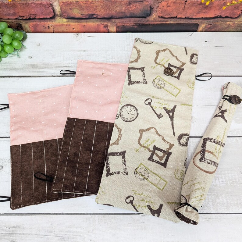 May include: Three fabric pencil cases with different patterns. One case is pink with white polka dots, another is brown with white stripes, and the third is beige with a pattern of keys, clocks, and Eiffel Towers.
