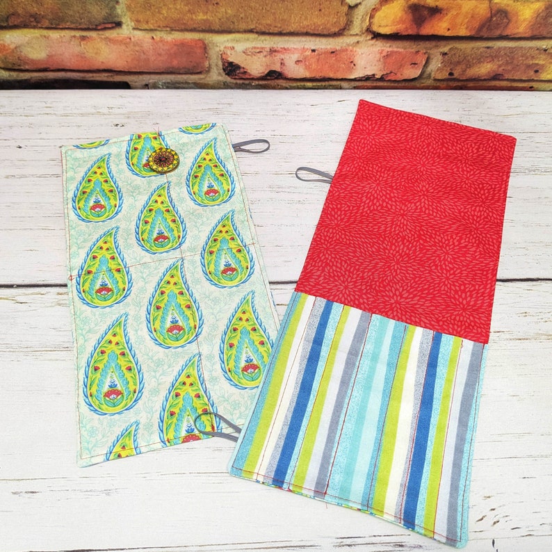 May include: Two fabric pouches with different patterns. One pouch has a paisley design with green and blue accents. The other pouch has a red fabric with a white and blue striped fabric underneath.