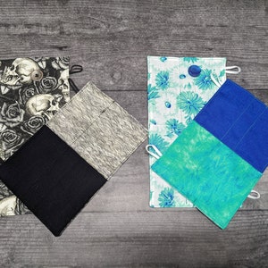 May include: Three different fabric pot holders. One is black with a skull and rose pattern, another is grey with a white pattern, and the last is blue and green with a floral pattern.