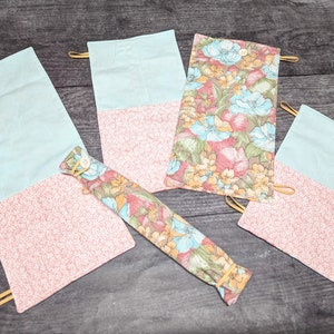 May include: Four fabric pouches with a floral pattern and a light blue colour. The pouches have a flap that folds over and closes with a snap. The pouches are made of a soft, cotton fabric and are ideal for storing small items.