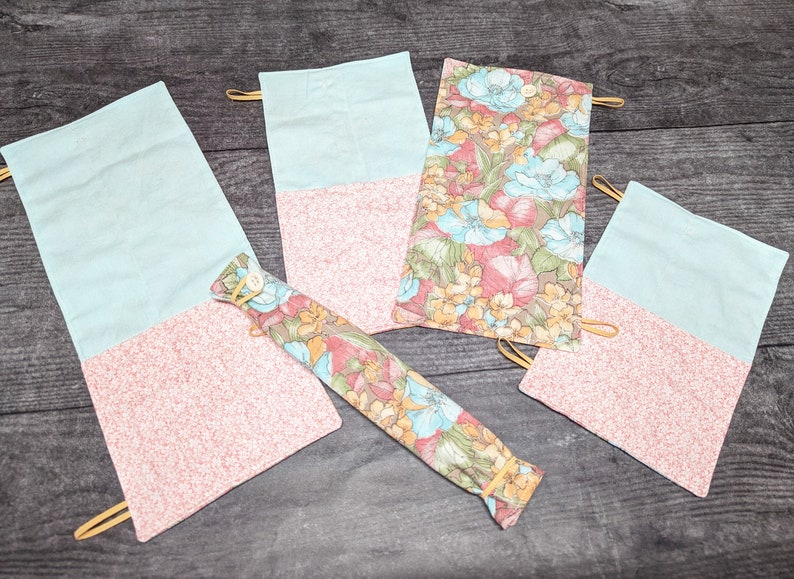 May include: Four fabric pouches with a floral pattern and a light blue colour. The pouches have a flap that folds over and closes with a snap. The pouches are made of a soft, cotton fabric and are ideal for storing small items.