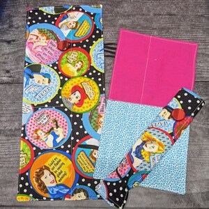 May include: A colourful fabric pencil case with a zipper closure. The case is decorated with a variety of images and text, including a woman with a red hat, a woman with a blue hat, and the text "T.G.I.F." and "The Queen is not accepting an audience today".