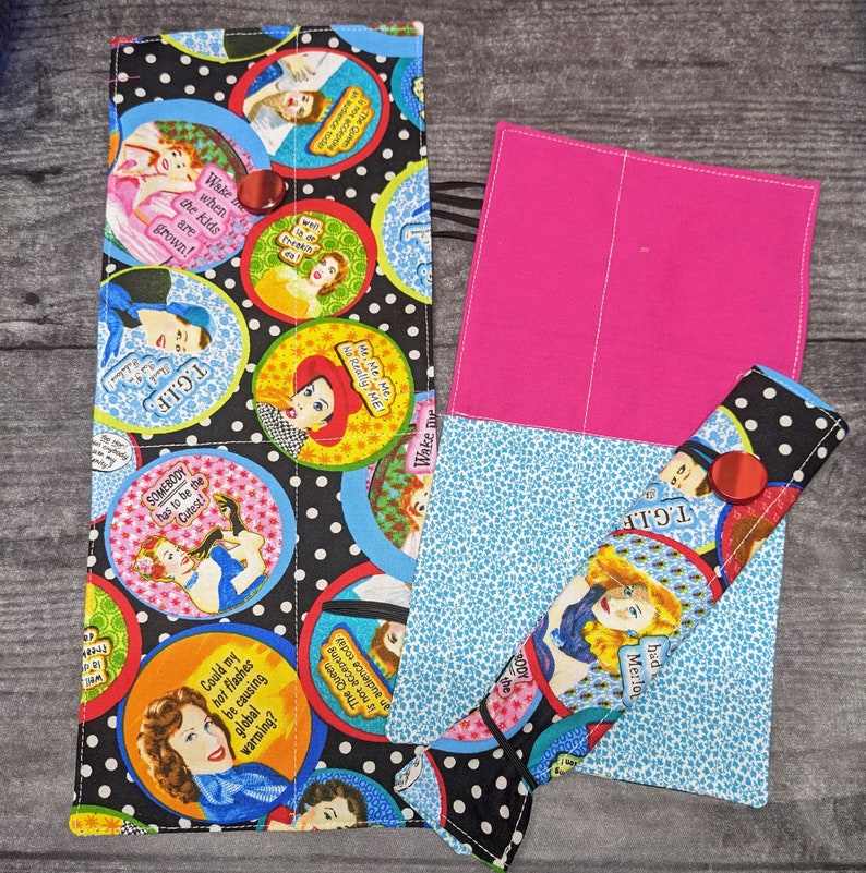 May include: A colourful fabric pencil case with a zipper closure. The case is decorated with a variety of images and text, including a woman with a red hat, a woman with a blue hat, and the text "T.G.I.F." and "The Queen is not accepting an audience today".