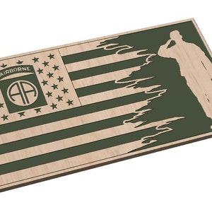 Könnte beinhalten: Holztafel mit einem stilisierten Design der amerikanischen Flagge, dem Text "AIRBORNE" und dem Abzeichen der 82. Luftlandedivision. Die Flagge geht in eine Silhouette eines salutierenden Soldaten über. Naturholz und olivgrüne Farbtöne.