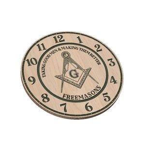 Peut inclure: Une horloge en bois avec une bordure verte et des chiffres romains. Au centre de l'horloge se trouve une boussole et une équerre, symbole de la franc-maçonnerie. Le texte "Taking good men & making them better" et "Freemasons" est inscrit autour de la boussole et de l'équerre.