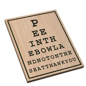May include: Wooden sign with a humorous eye chart that reads "Pee in the bowl and not on the seat thank you". The sign is made by American South Designs.