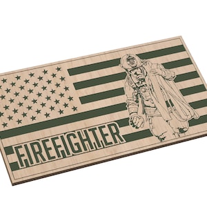 Könnte beinhalten: Holzschild mit einem grünen amerikanischen Flaggen-Design und dem Wort "FIREFIGHTER" in grünen Buchstaben. Im Zentrum der Flagge ist ein Feuerwehrmann abgebildet.