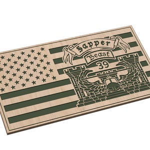 Puede incluir: Una bandera estadounidense de madera con un emblema militar verde que presenta un castillo, alas y el texto "Sapper Beast 39".