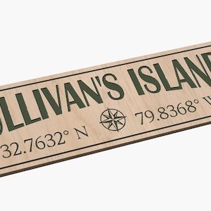 以下が含まれることがあります： 緑色の文字で「SULLIVAN'S ISLAND」と書かれた木製の看板。看板には「32.7632° N 79.8368° W」の座標とコンパスローズも記されています。