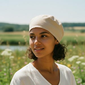 Puede incluir: Un gorro de color beige claro liso hecho de una tela suave, con una corona redondeada y una banda ajustada que se asienta firmemente alrededor de la cabeza. El gorro tiene una textura suave y sencilla con un tono neutro y funcional.