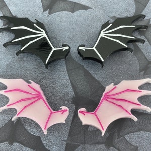 Puede incluir: Dos pares de alas decorativas. Un par es negro con vetas blancas y el otro par es rosa con vetas blancas.