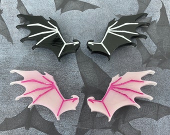 May include: Two pairs of decorative wings. One pair is black with white veins and the other pair is pink with white veins.