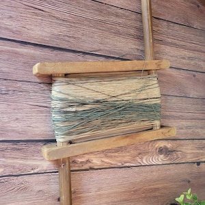 May include: A wooden spool with a handle on each side, holding a bundle of twine. The twine is a mix of natural beige and green colors.
