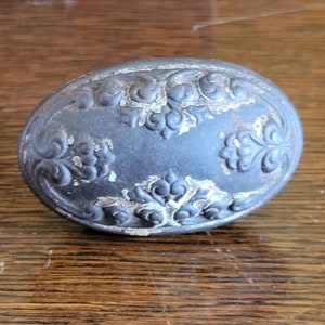 May include: A black oval-shaped door knob with a decorative floral design. The knob has a worn, aged look with some silver paint showing through.