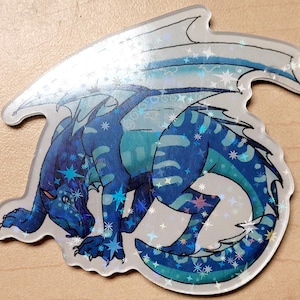 May include: A holographic sticker featuring a blue dragon with a detailed design. The dragon has a mix of dark and light blue scales, with star-shaped accents. The wings are a lighter shade of blue, and the sticker has a glossy finish.