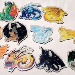 May include: A collection of colorful dragon-themed stickers. The stickers feature various dragon designs in shades of green, blue, yellow, orange, and black. Some dragons have wings, and some are depicted with books or scrolls. The stickers are on a white surface.