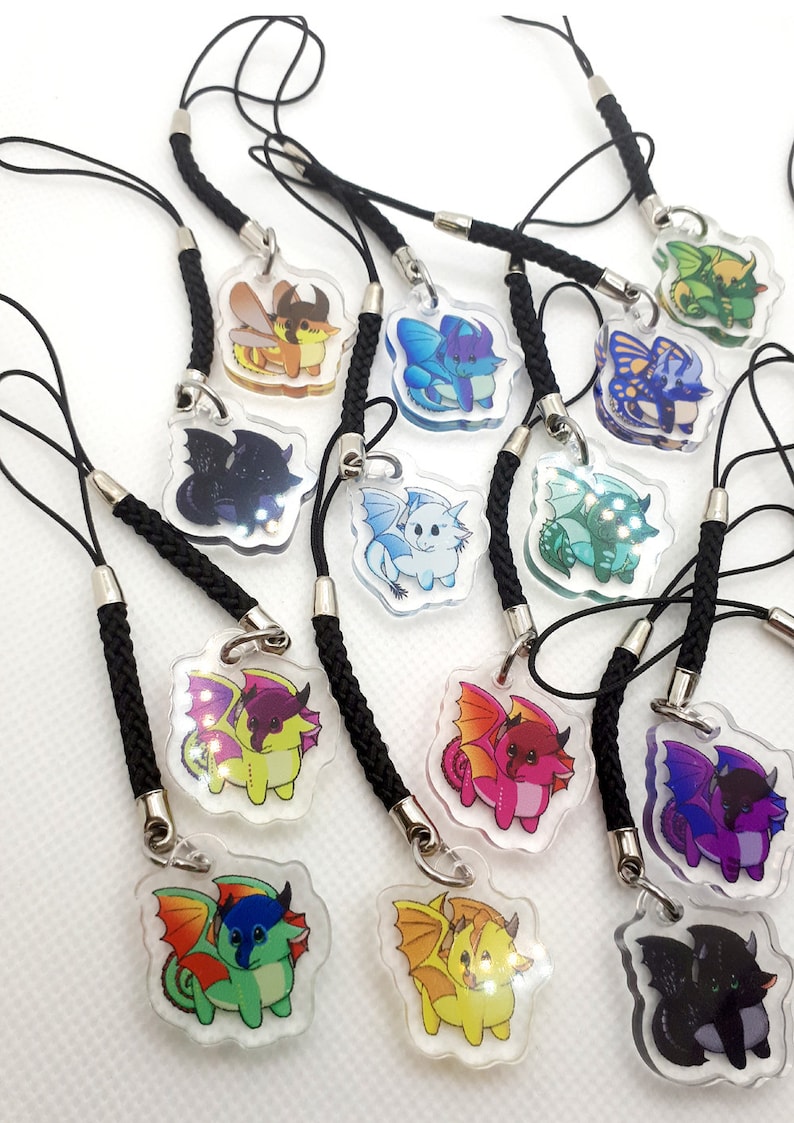 May include: A collection of 12 colorful dragon phone charms with black braided lanyards. Each charm features a different dragon design with a clear acrylic background.