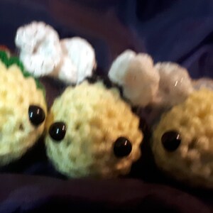 Puede incluir: Tres peluches de abeja de crochet con alas blancas y ojos negros. Las abejas son amarillas, verdes y azules.
