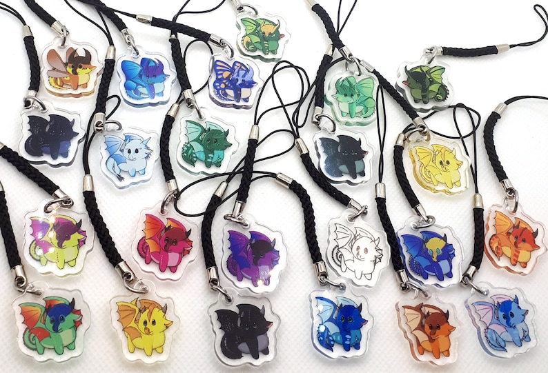 May include: A collection of 18 colorful dragon phone charms. Each charm features a cartoon dragon with wings and a tail. The charms are made of clear acrylic and have a black cord attached.