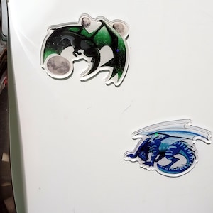 May include: Three dragon-themed stickers. One features a black dragon with green wings and two moons. The other shows a blue dragon with white wings. Both are on a white background.