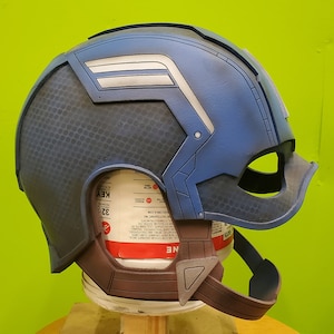 May include: A blue and gray Captain America helmet with a white star and stripes on the side. The helmet is made of plastic and has a textured surface.