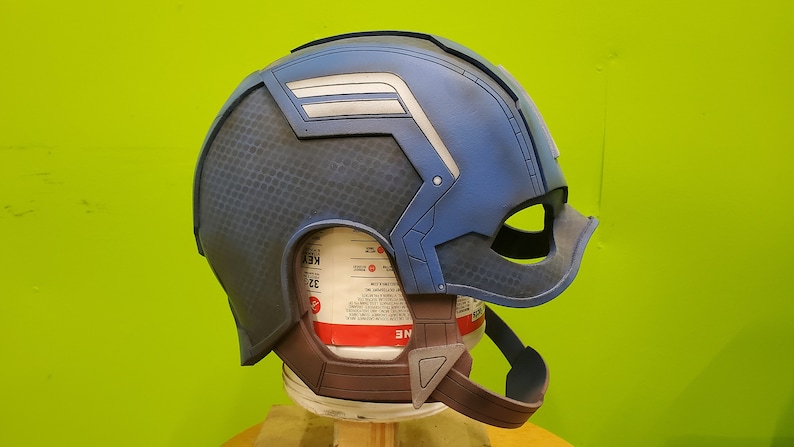 May include: A blue and gray Captain America helmet with a white star and stripes on the side. The helmet is made of plastic and has a textured surface.