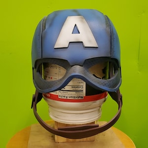 May include: A blue and white Captain America helmet with a red and white strap. The helmet is made of plastic and has a distressed look.
