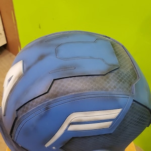 May include: A blue and gray helmet with a white stripe and a textured surface.
