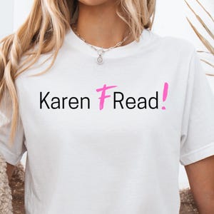 Puede incluir: Camiseta blanca con el texto "Karen F Read!" en negro y rosa. La camiseta se usa con pantalones cortos de mezclilla y una rebeca beige. La persona está haciendo el signo de la paz.