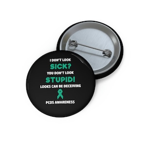 May include: Black button with white text that reads "I don't look sick? You don't look stupid! Looks can be deceiving. PCOS Awareness." A teal ribbon is below the text.
