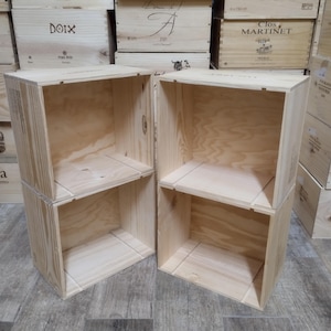 Może przedstawiać: Cztery niewykończone drewniane skrzynie, ułożone parami, z otwartymi frontami i wewnętrznymi półkami. Skrzynie wykonane są z jasnego drewna, z widocznym usłojeniem. Tło pokazuje inne drewniane skrzynie z tekstem.