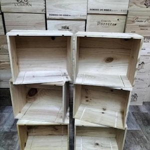 Op de afbeelding: Verschillende onafgewerkte houten kisten gestapeld. De kisten zijn rechthoekig met een natuurlijke houtnerf. De achtergrond toont meer houten kisten met tekst, wat wijst op een opslag- of displaythema.