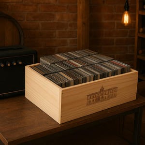 May include: A wooden box filled with rectangular items, possibly coasters or tiles, sits on a dark wooden table. A black amplifier with gold knobs and a handle is to the left. A wooden barrel and brick wall are in the background.