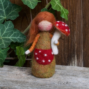 Felted girl figurine holding a white dotted red mushroom.