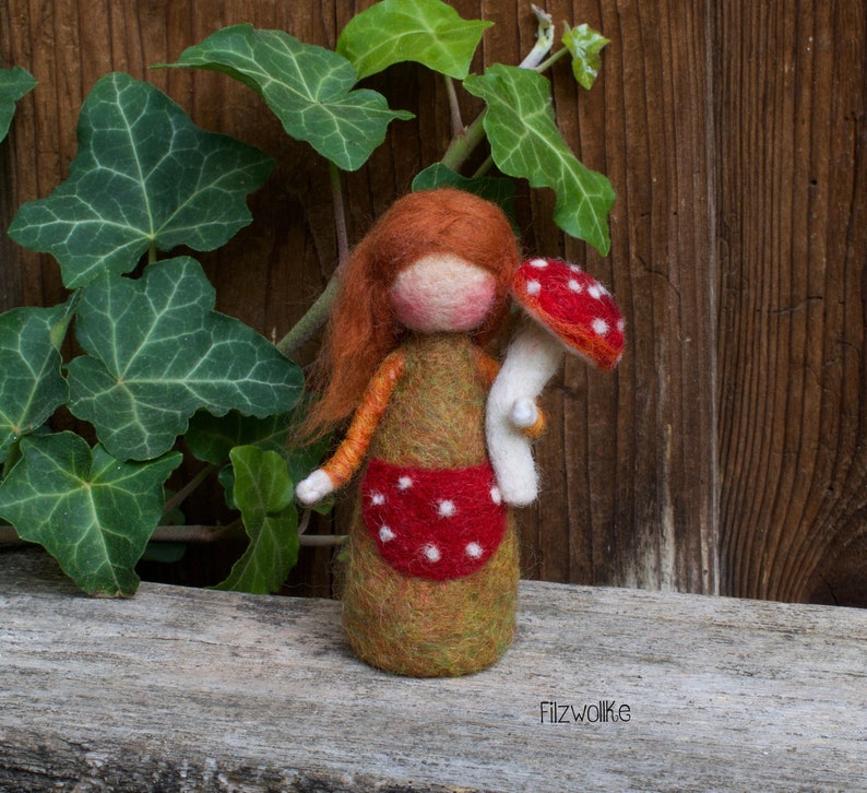 Felted girl figurine holding a white dotted red mushroom.
